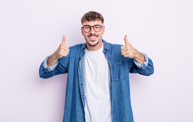 Jovem bonito sorrindo, parecendo feliz, positivo, confiante e bem-sucedido, com os dois polegares para cima