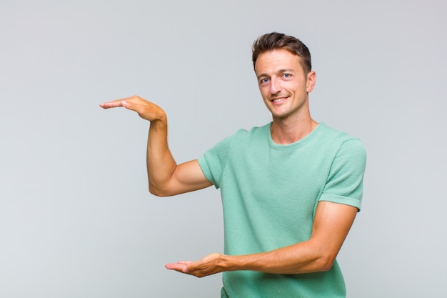 Jovem bonito sorrindo, sentindo-se feliz, positivo e satisfeito, segurando ou mostrando o objeto ou conceito no espaço da cópia