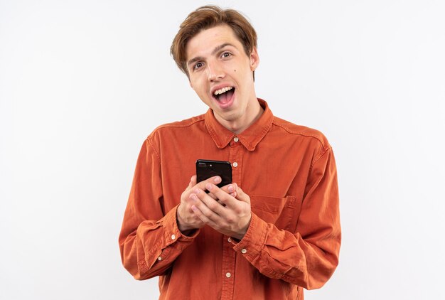 Foto jovem bonito surpreso de camisa vermelha, segurando o telefone isolado na parede branca