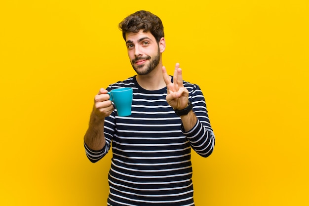 Jovem bonito, tomando um café contra a parede laranja