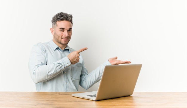 Jovem bonito, trabalhando com seu laptop animado segurando uma palma da mão copyspace.