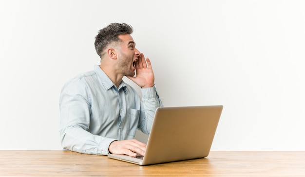 Jovem bonito, trabalhando com seu laptop, gritando e segurando a palma da mão perto da boca aberta.