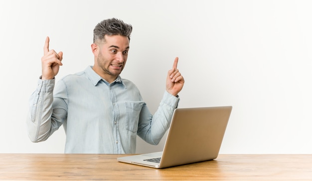 Jovem bonito, trabalhando com seu laptop indica com os dois dedos da frente, mostrando um espaço em branco.