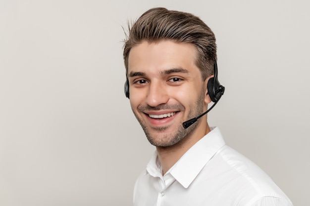 Jovem bonito trabalhando em um call center com fones de ouvido e sorrindo