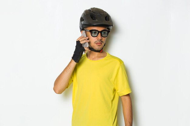 Jovem bonito usando capacete de ciclista, usando telefone celular isolado no fundo branco