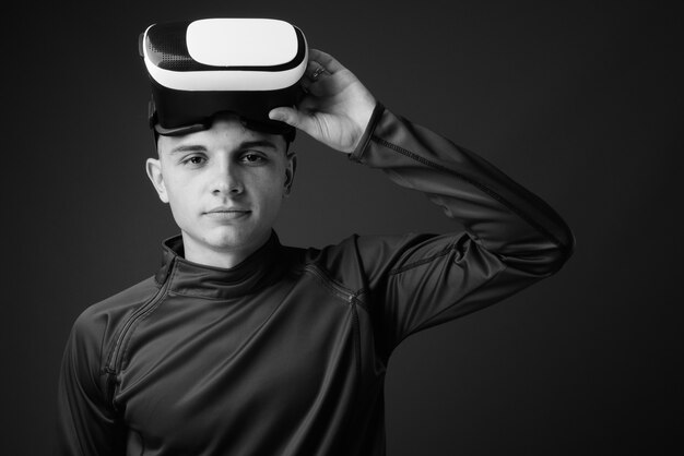 Jovem bonito usando fone de ouvido de realidade virtual contra parede cinza. preto e branco