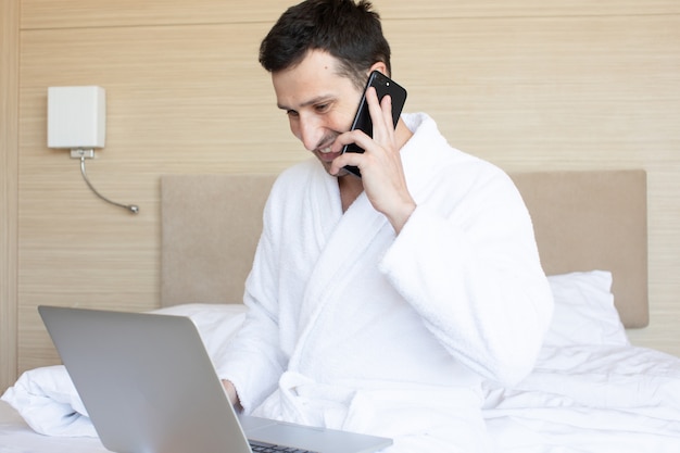 Jovem bonito usando laptop enquanto está sentado na cama.