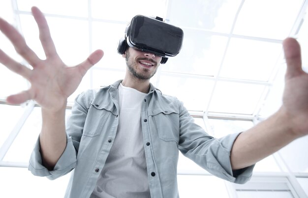 Jovem bonito usando óculos de realidade virtual acenando alto com luvas de controle remoto