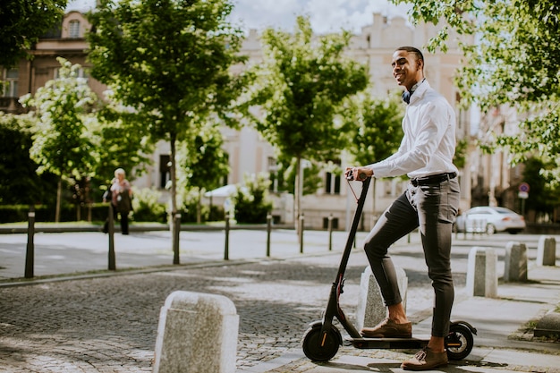 Foto jovem bonito usando scooter elétrico em uma rua