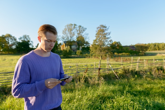 Jovem bonito usando telefone celular em uma planície pacífica e gramada com a natureza