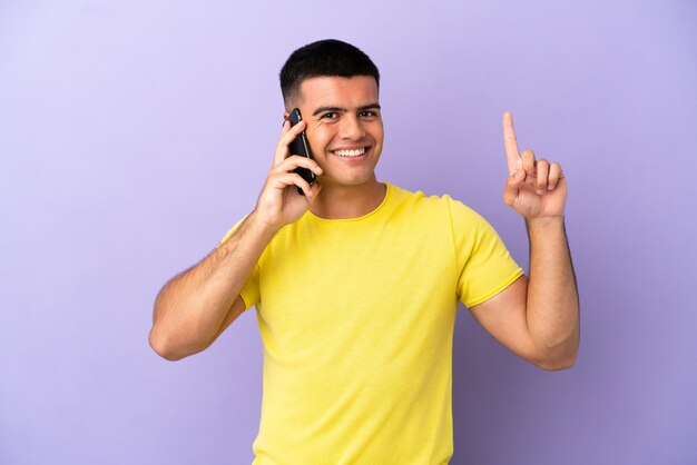 Jovem bonito usando telefone celular sobre fundo roxo isolado apontando para uma ótima ideia