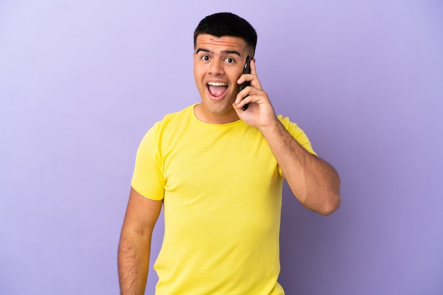 Jovem bonito usando telefone celular sobre fundo roxo isolado com expressão facial surpresa