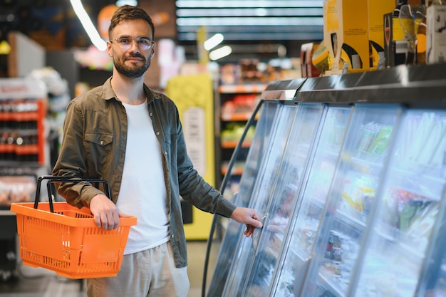 Jovem bonito verifica os frigoríficos para alimentos congelados no supermercado