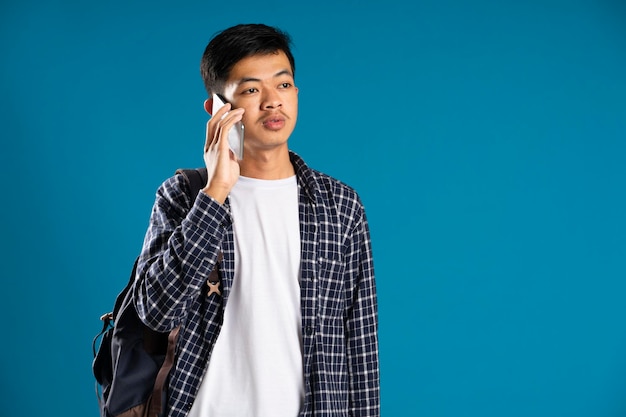 Jovem bonito vestindo camisa e bolsa está no telefone de alguém em fundo azul