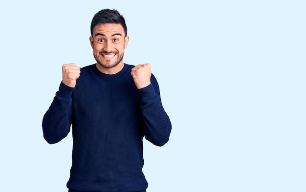 Foto jovem bonito vestindo roupas casuais comemorando surpreso e surpreso pelo sucesso com os braços levantados e olhos abertos. conceito de vencedor.