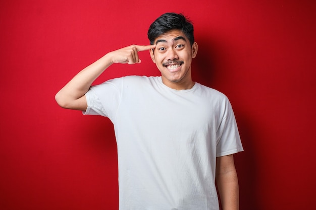 Jovem bonito vestindo uma camisa casual sorrindo apontando para a cabeça com os dedos das duas mãos, ótima ideia ou pensamento, boa memória sobre fundo vermelho