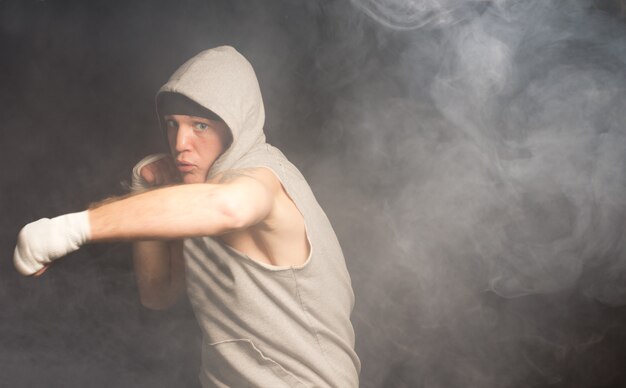 Jovem boxeador ágil jogando seu peso atrás de um soco com um olhar severo de terminação em um ambiente escuro e esfumaçado