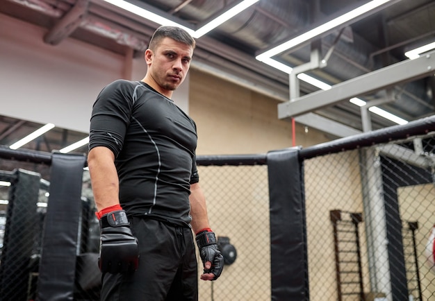 Jovem boxeador de preto veste olhando para a câmera com confiança, antes de lutar, pratica o poder e a força. MMA, conceito de kickboxing