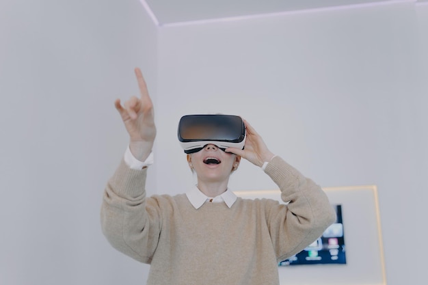 Jovem branca em óculos VR no escritório futurista Garota em óculos VR está apontando com o dedo