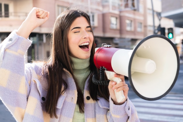 Jovem brasileira ao ar livre gritando através de um megafone para anunciar algo em posição lateral