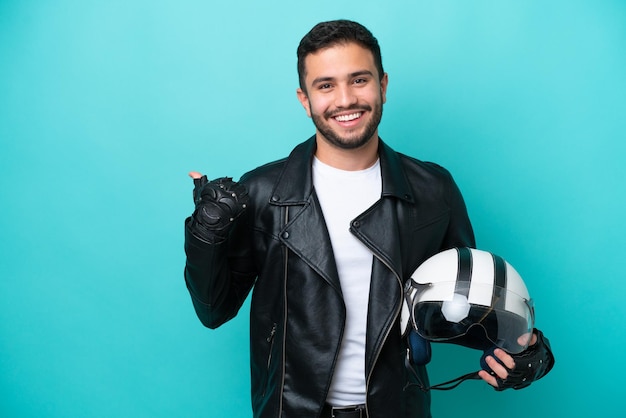 Jovem brasileira com capacete de moto isolado em fundo azul apontando para o lado para apresentar um produto