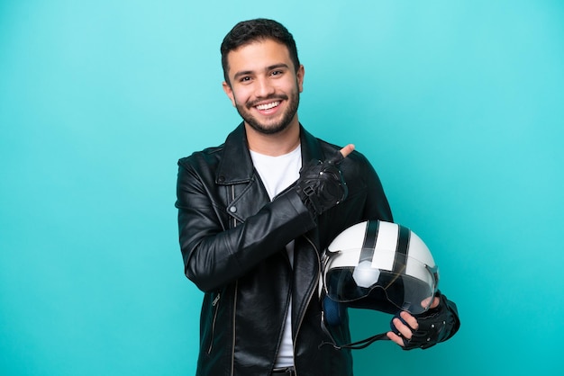 Jovem brasileira com capacete de moto isolado em fundo azul apontando para o lado para apresentar um produto