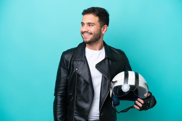 Jovem brasileira com capacete de moto isolado em fundo azul olhando para o lado e sorrindo