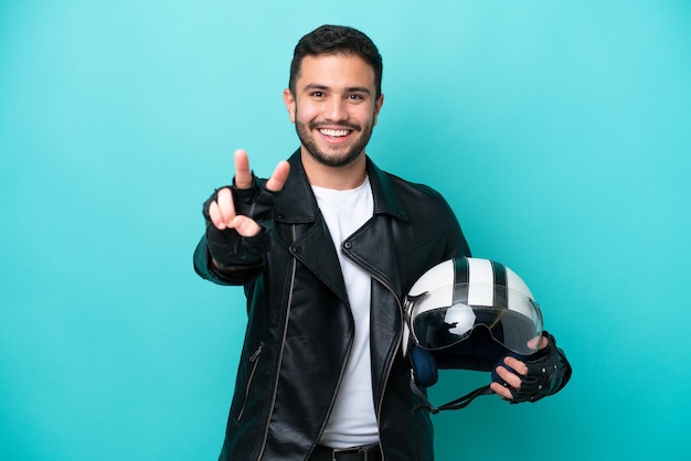 Jovem brasileira com capacete de moto isolado em fundo azul sorrindo e mostrando sinal de vitória