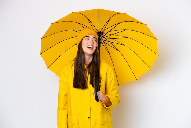 Jovem brasileira com casaco à prova de chuva e guarda-chuva isolado no fundo branco rindo