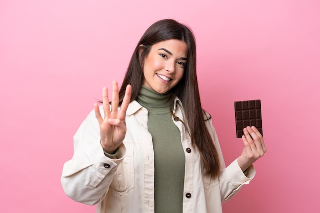 Jovem brasileira com chocolate isolado em fundo rosa feliz e contando quatro com os dedos