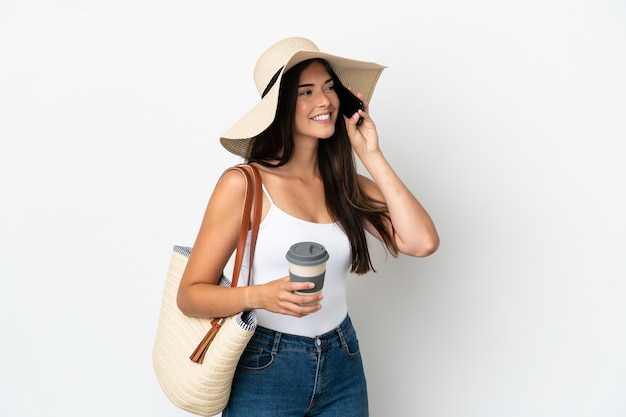 Jovem brasileira com Pamela segurando uma sacola de praia isolada no fundo branco segurando um café para levar e um celular