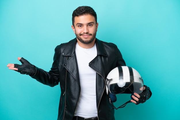 Jovem brasileira com um capacete de moto isolado em fundo azul com dúvidas ao levantar as mãos