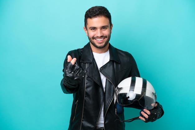 Jovem brasileira com um capacete de moto isolado em fundo azul, fazendo gesto de dinheiro