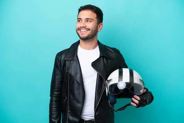 Jovem brasileira com um capacete de moto isolado em fundo azul, pensando em uma ideia enquanto olha para cima