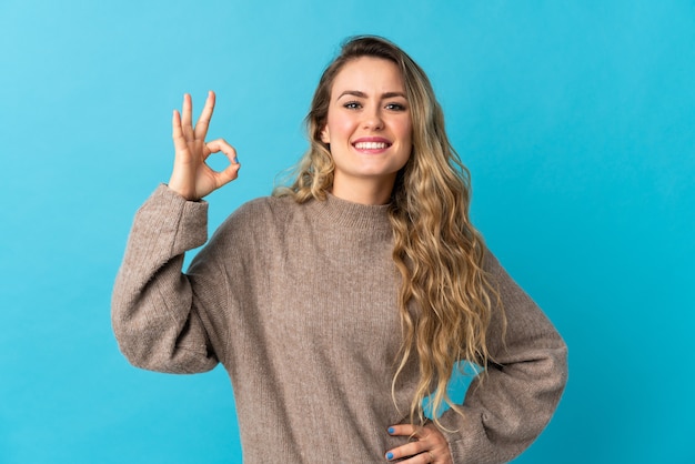 Jovem brasileira isolada em azul mostrando sinal de ok com os dedos