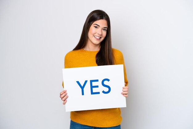 Foto jovem brasileira isolada em fundo branco segurando um cartaz com texto sim com expressão feliz