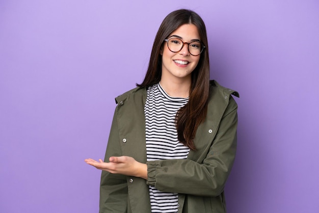 Jovem brasileira isolada em fundo roxo apresentando uma ideia enquanto olhava sorrindo para