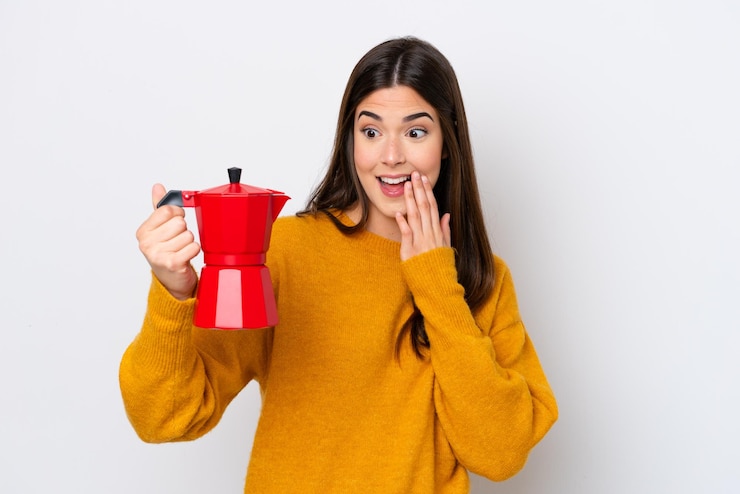 Foto jovem brasileira segurando a cafeteira isolada no fundo branco com surpresa e expressão facial chocada