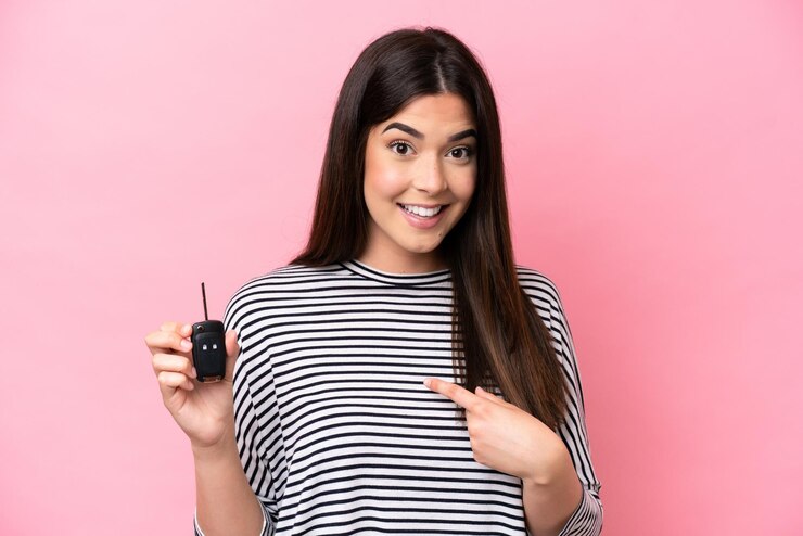 Foto jovem brasileira segurando as chaves do carro isoladas em fundo rosa com expressão facial de surpresa