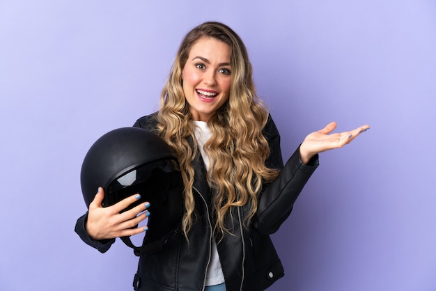 Jovem brasileira segurando um capacete de moto isolado em roxo com expressão facial chocada