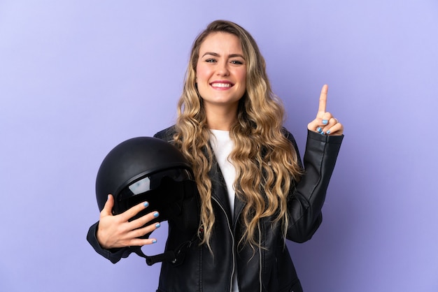 Jovem brasileira segurando um capacete de motociclista isolado no roxo apontando uma ótima ideia