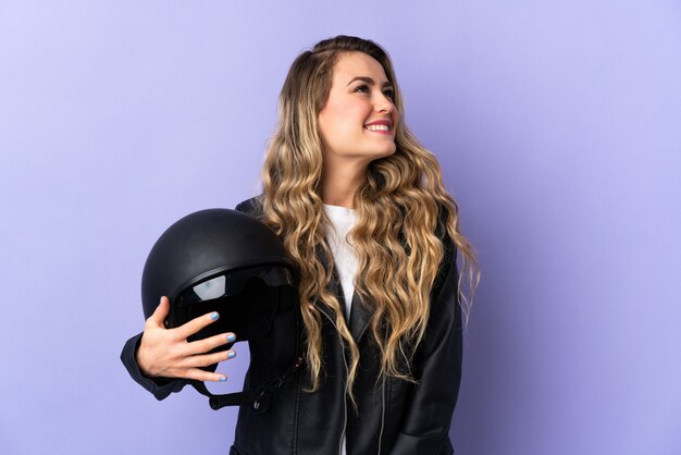 Jovem brasileira segurando um capacete de motociclista isolado no roxo pensando em uma ideia enquanto olha para cima