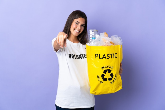 Jovem brasileira segurando uma sacola cheia de garrafas plásticas para reciclar isolada
