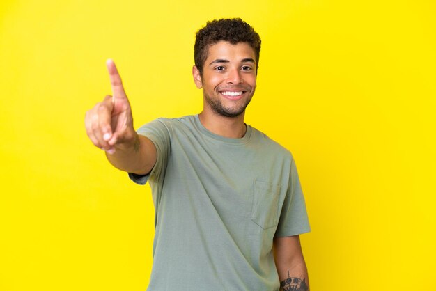 Foto jovem brasileiro bonito isolado em fundo amarelo mostrando e levantando um dedo