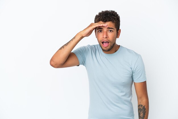 Foto jovem brasileiro bonito isolado no fundo branco, olhando para longe com a mão para procurar algo