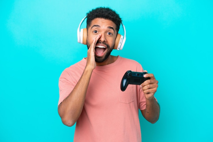 Foto jovem brasileiro brincando com um controlador de videogame isolado em fundo azul gritando com a boca aberta