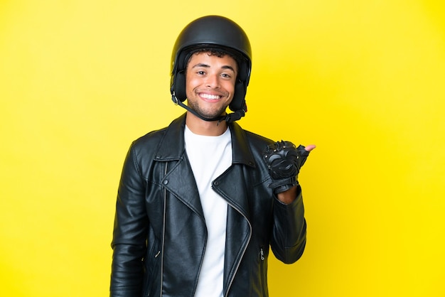 Jovem brasileiro com capacete de moto isolado em fundo amarelo apontando para o lado para apresentar um produto