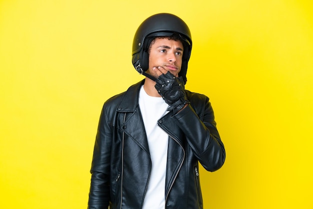 Jovem brasileiro com capacete de moto isolado em fundo amarelo com dúvidas