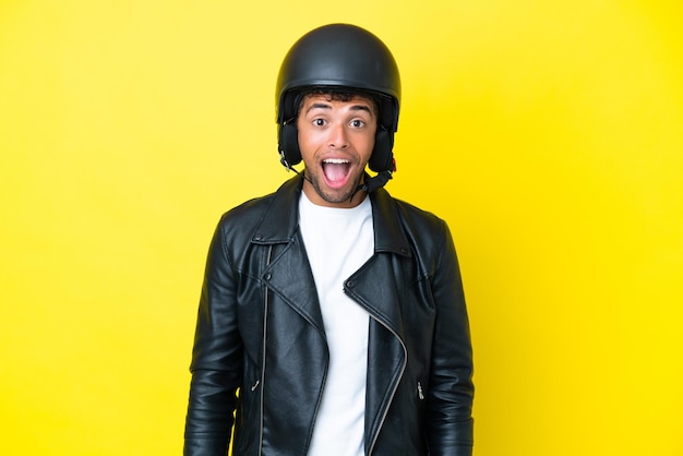 Jovem brasileiro com capacete de motociclista isolado em um fundo amarelo com expressão facial surpresa