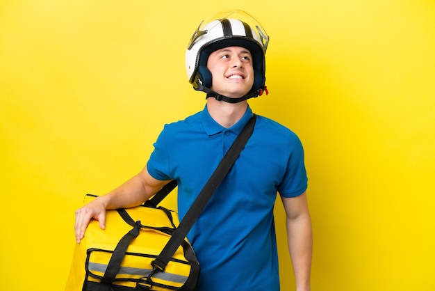 Jovem brasileiro com mochila térmica isolada em fundo amarelo pensando em uma ideia enquanto olha para cima